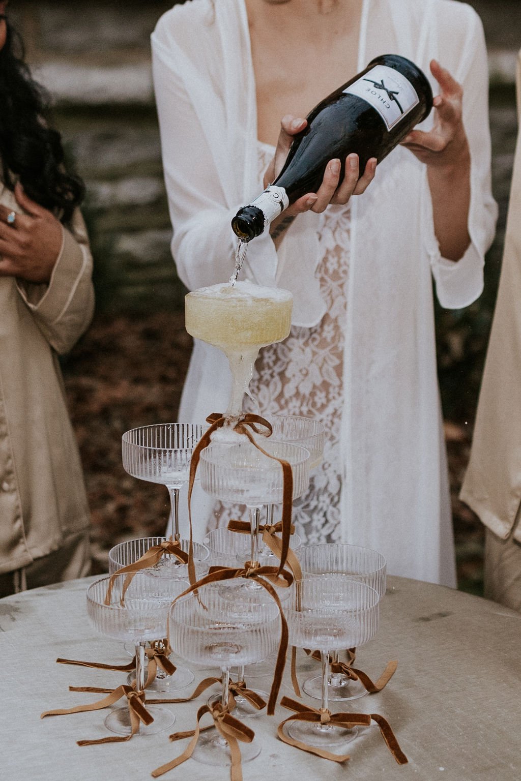 Bride pouring champagne tower with ribbon-tied coupe glasses